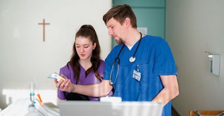 Praxisanleiter Tobias Edler zeigt einer Pflegesch&uuml;lerin den Umgang mit einem digitalen Infrarot-Fieberthermometer